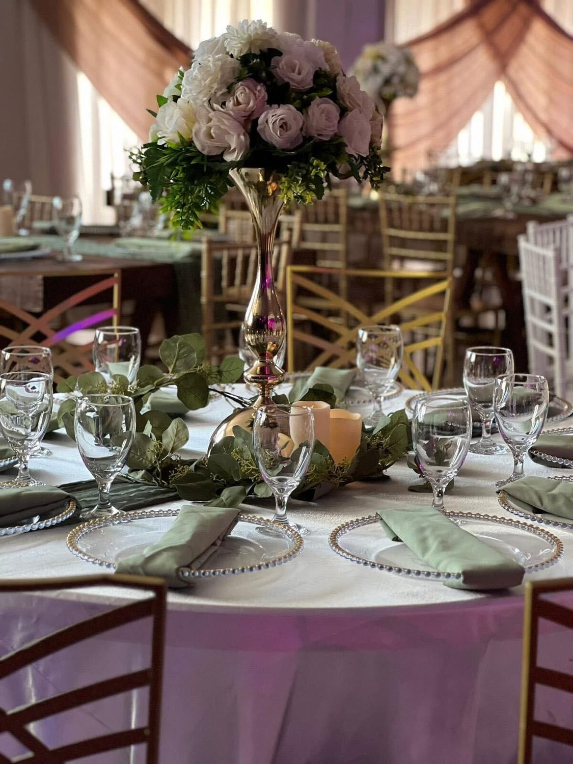 A sage and ivory table with a tall floral centerpiece